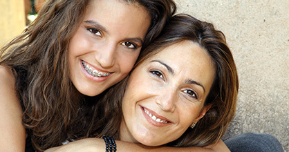 Teen daughter with arm around mother, both smiling 