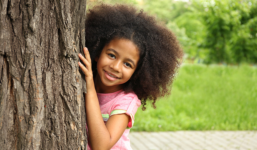 Shy little girl peering out from behind a tree.