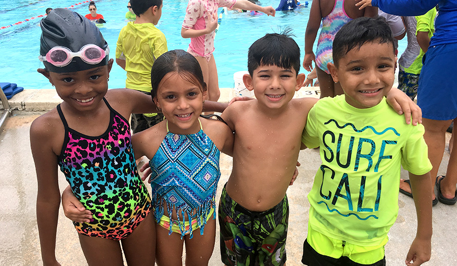 Smiling children in swimsuits standing by a pool