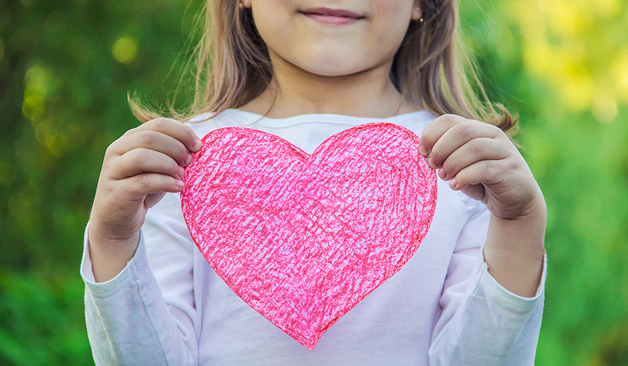 Young girl holding up a paper valentine heart.