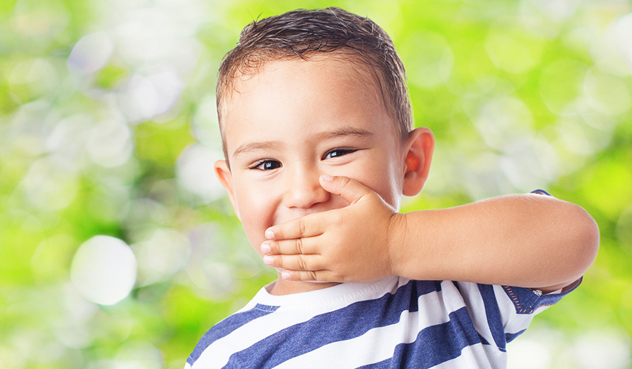 Little boy holding his hand over his mouth.