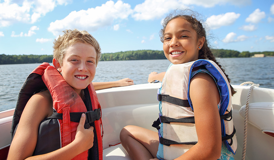 Happy girl and boy wearing life jackets on a boat.