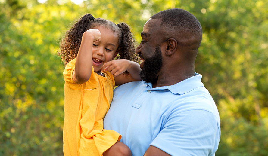 Papá sonriente con su niña pequeña en brazos.