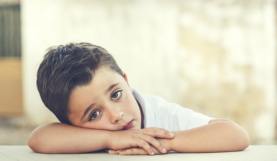 Un niño pequeño, aburrido, apoya la cabeza sobre sus brazos.