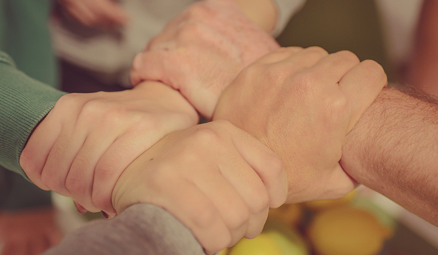 Four hands interlocking together on wrists.