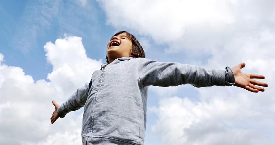 A young Latino boy spreads his arms in joy. 