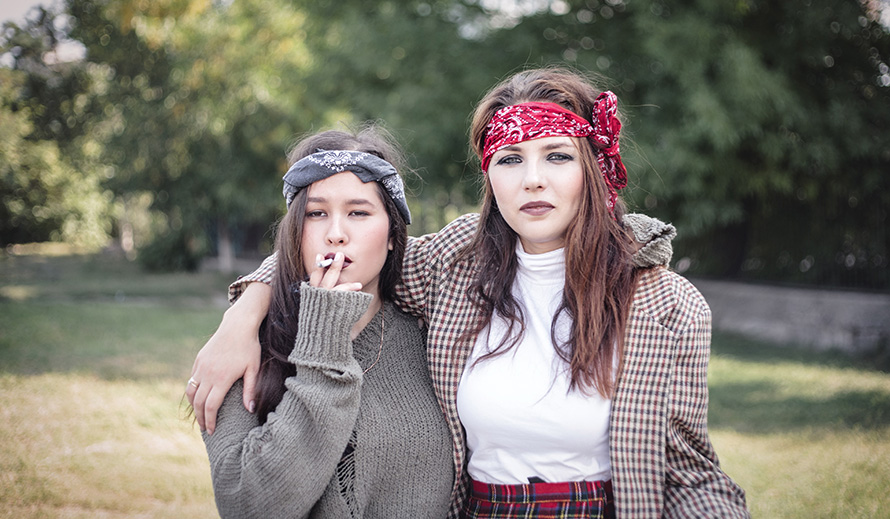 Dos niñas informalmente vestidas caminan por la calle llevando cigarrillos.