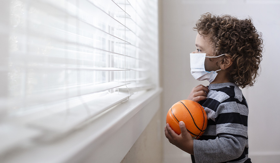 A young child looks longingly out the window during coronavirus pandemic. 