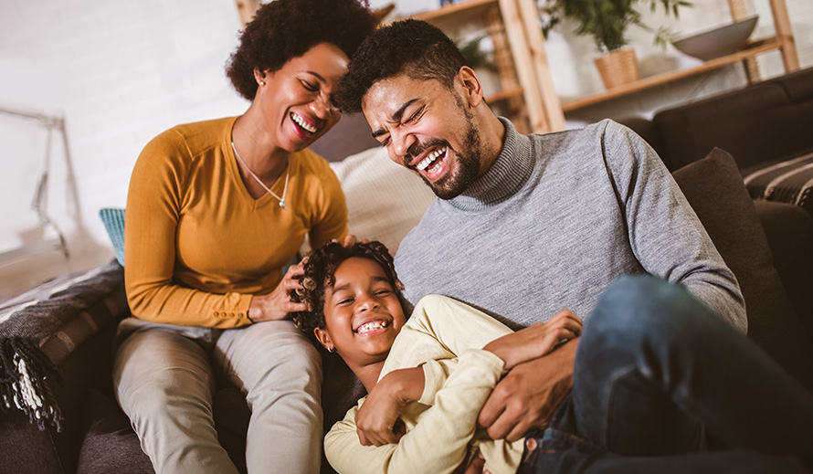 Padre afroamericano y madre le hacen cosquillas a su hija en casa.