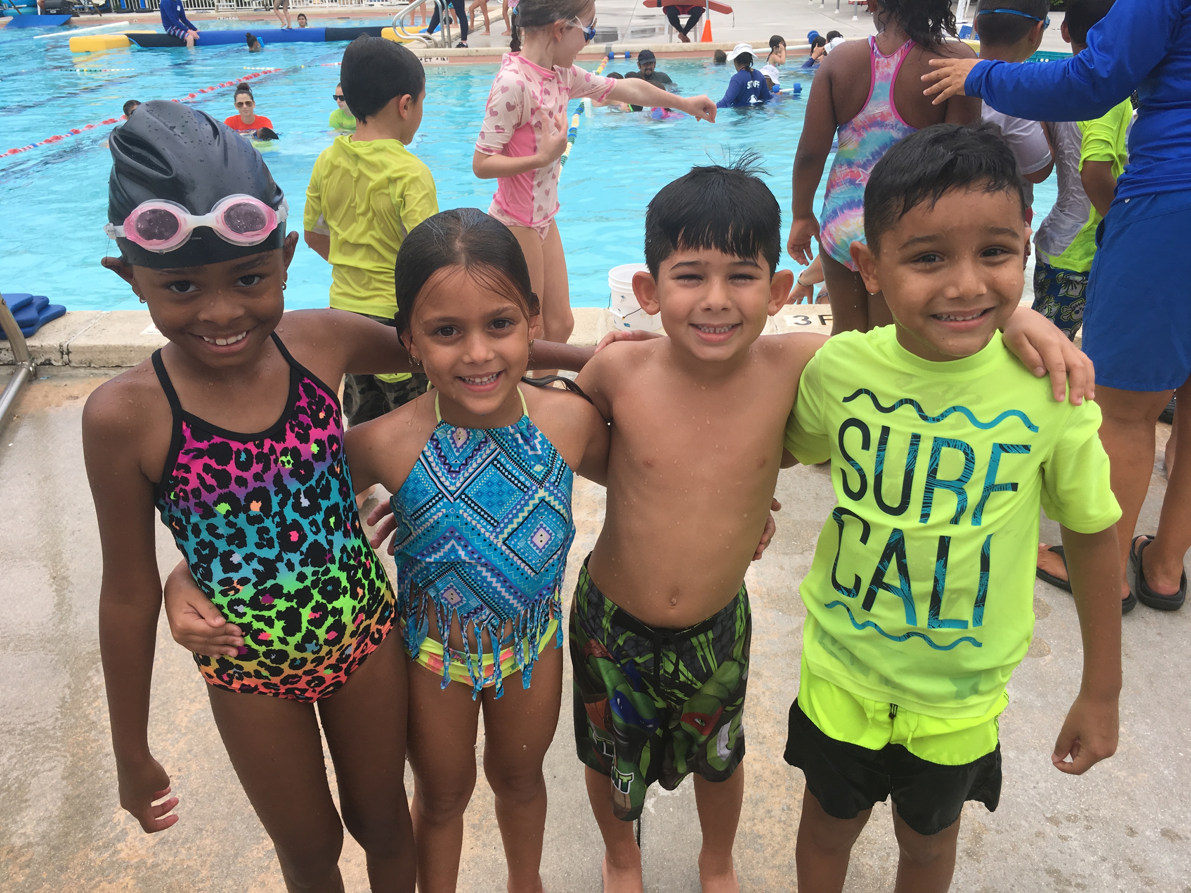 Smiling children in swimsuits standing by a pool