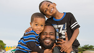 African American father carrying two boys on his shoulders.^