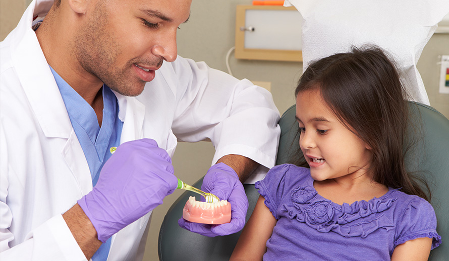 Dentist showing a little girl how to brush her teeth