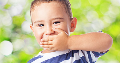 Little boy holding his hand over his mouth.