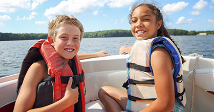 Happy girl and boy wearing life jackets on a boat.