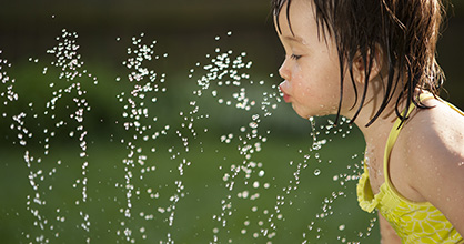 Little girl cools off by drinking from sprinkler.