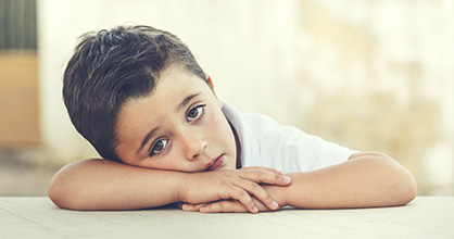 A bored little boy rests his head on his arms