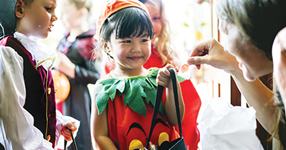 A little girl dressed as a pumpkin gets candy on Halloween.