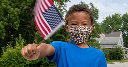  Un niño ondea una bandera estadounidense con una máscara puesta.