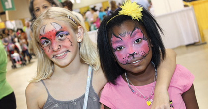 Two smiling young girls with painted faces, one a demon and one a cat, at the Family Expo.