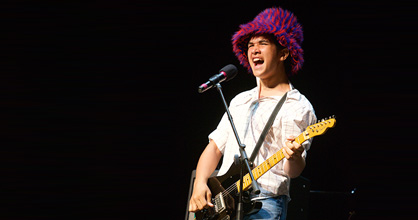 Teen boy onstage singing and playing electric guitar